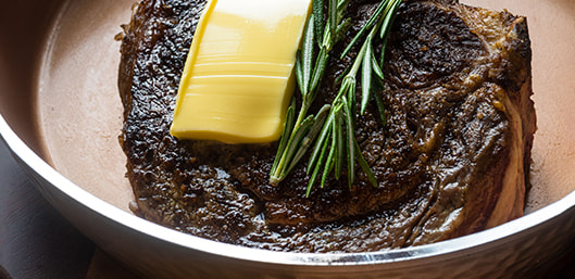 Cooked steak topped with butter and rosemary inside Gotham Steel™ Hammered Pan